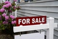 Red and white for sale sign in front of a grey house