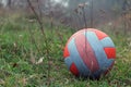Red-white soccer ball on grass in a park with foggy gloomy rainy weather