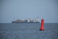 A red and white steel navigational floating buoy and a lrge containership in the blue sea water, drift with the sea wave, among Royalty Free Stock Photo