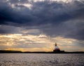 A red and white lighthouse on an island surrounded by storm clouds