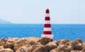 Red and white striped sea safety beacon fixed on the rocks in port with the water horizon in the background