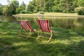 Red and white striped sun loungers standing in the lawn on the natural bank of a river, inviting idyll on a sunny summer day, copy Royalty Free Stock Photo