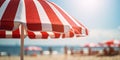 Close up of red and white striped sun parasol with blurry beach on sunny day in background Royalty Free Stock Photo