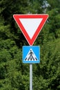Red and white triangle give way or yield road sign above pedestrians crossing blue and white rectangle small road sign