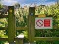 A red and white warning sign on a stile on the Northumberland Coast Path warns walkers of the danger of overhead power lines