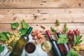 Red and white wine glasses and bottles on wooden background, copy space. Fresh grapes and grape leaves as decoration