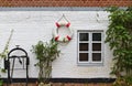 Red and whitewashed brick wall with window, green bushes, red and white life buoy and historic anchor winch Royalty Free Stock Photo