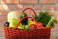 Red wicker plastic basket filled to the top with green, yellow, red and dark vegetables on a brick wall background Royalty Free Stock Photo