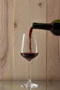 Red wine being poured into a glass bottle of red wine with a brilliant glass on a wooden background on a glass stand