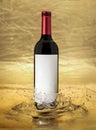 Red wine bottle with blank label immersed in a golden splash Royalty Free Stock Photo
