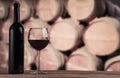 Red wine bottle with glass on the background of oak barrels. Wine background Royalty Free Stock Photo