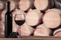 Red wine bottle with glass on the background of oak barrels. Wine background Royalty Free Stock Photo