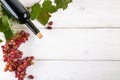 Red wine bottle with grapes green leaves on white wooden table background Royalty Free Stock Photo