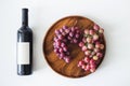 Red wine bottle and large burgundy fresh grapes on wooden dish on white background, copy space flat lay, top view Royalty Free Stock Photo