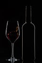 Red wine bottle and splashing wine in glass on dark background Royalty Free Stock Photo