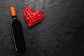 Red wine bottle with wicker decorative heart on black stone background. Valentines day love celebration. Copy space Royalty Free Stock Photo