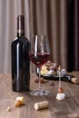 A bottle of red wine, a glass with red wine, a board with snacks, cheese and grapes