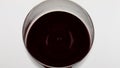Red wine droplet falling rippling in goblet closeup. Smooth beverage surface