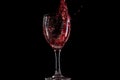 Red wine falls into a glass and creates splash and splashes on a black background