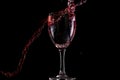 Red wine falls into a glass and creates splash and splashes on a black background