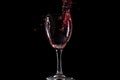 Red wine falls into a glass and creates splash and splashes on a black background