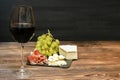 Red wine in glass, bottle, brie cheese, blue cheese, grapes, jamon meat, salami on black slate board on wooden table Royalty Free Stock Photo