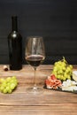 Red wine in glass, bottle, brie cheese, blue cheese, grapes, jamon meat, salami on black slate board on wooden table Royalty Free Stock Photo