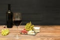 Red wine in glass, bottle, brie cheese, blue cheese, grapes, jamon meat, salami on black slate board on wooden table Royalty Free Stock Photo