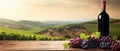 Red wine glass, bottle and fresh red grapes on wooden table over background of panoramic view of vineyards at sunset. Royalty Free Stock Photo