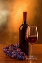 Red wine glass and bottle with grapes on wooden table and golden background Royalty Free Stock Photo