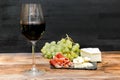 Red wine in glass, brie cheese, blue cheese, grapes, jamon meat, salami on black slate board on wooden table, alcohol Royalty Free Stock Photo