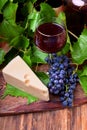 Red wine in a glass, a bunch of blue Isabella grapes and a piece of Maasdam cheese Royalty Free Stock Photo