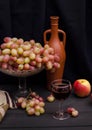 Red wine in a glass with grapes in a vase on a wooden table on a black cloth background with an old bottle. For wine advertising Royalty Free Stock Photo