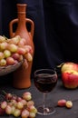 Red wine in a glass with grapes in a vase on a wooden table on a black cloth background with an old bottle. For wine advertising Royalty Free Stock Photo