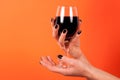 Female hand with black nails holding wine glass on orange background in studio