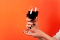 Red wine in glass holding young girl in hand with black nail isolated on orange background Royalty Free Stock Photo