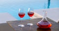 Red wine glasses at the swimming pool. Two wineglasses and carafe on turquoise water background Royalty Free Stock Photo