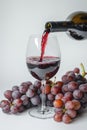 Red wine poured into glass and grapes on white background. AI Generated Royalty Free Stock Photo