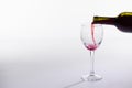 Red wine pouring from bottle into big glass on white background with copy space Royalty Free Stock Photo