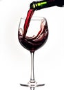 Red wine pouring down from a bottle into a glass, over white background Royalty Free Stock Photo