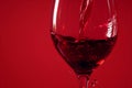 Red wine pouring in glass on red background closeup. Glass of wine, drink for celebrating, date, family dinner, party. Wine shop,