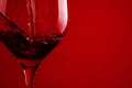 Red wine pouring in glass on red background closeup. Glass of wine, drink for celebrating, date, family dinner, party. Wine shop,