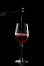 Red wine pouring into a glass with drops on black background