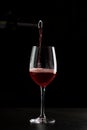 Red wine pouring into a glass with drops on black background Royalty Free Stock Photo