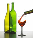 Red wine pouring into glass with two green bottles in background Royalty Free Stock Photo