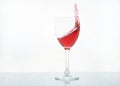 Red wine pouring motion in glass goblet on white glass background. Splash with a drop of red wine or tasty red liquid. splatter of Royalty Free Stock Photo