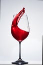 Red wine splash in the delicate elegant wineglass standing against light background.