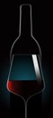 Red wine in a wine glass is seen in dramatic lighting in front of an unopened wine bottle