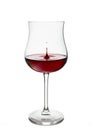 Red wine in wineglass isolated on white background. Drop falls into glass and creates splash and wave on surface of red wine Royalty Free Stock Photo