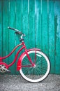 Red women`s retro style bicycle leaning against a bright blue green wooden fence. Royalty Free Stock Photo